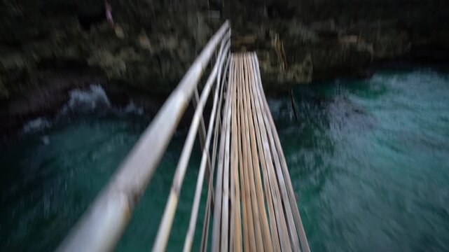 First person view walking on narrow bamboo bridge above clear turquoise sea in Carabao Island near Boracay Philippines with legs and sandals visible approaching rocky shore