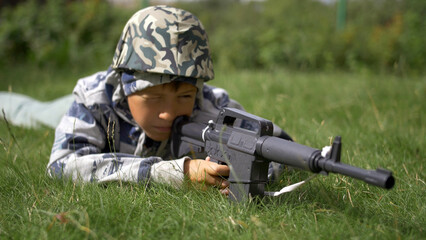 Fototapeta premium boy in camoflauge playing war shoots a toy gun, have fun and enjoy