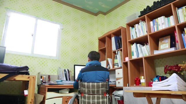 한국의 사무실에서 휠체어에 앉아 모니터를 보며 컴퓨터 작업에 집중하고 있는 남성의 뒷모습 핸드헬드 브이로그 영상