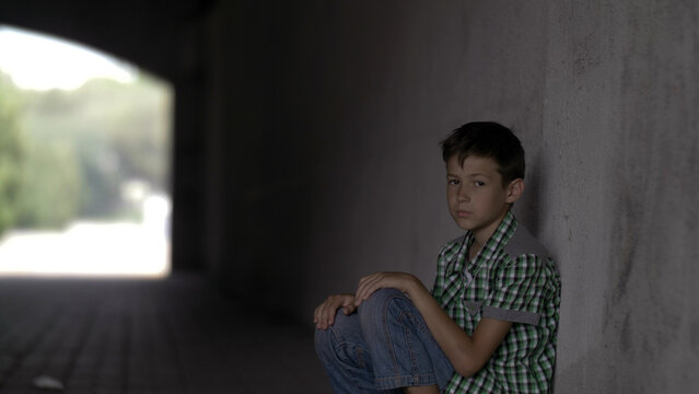 offended abandoned boy sits in a tunnel on the floor, looks at the camera, have fun and enjoy