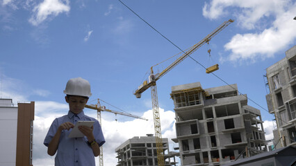 builder boy stands among builder cranes using tablet, boy plays a builder, have fun and enjoy © vla