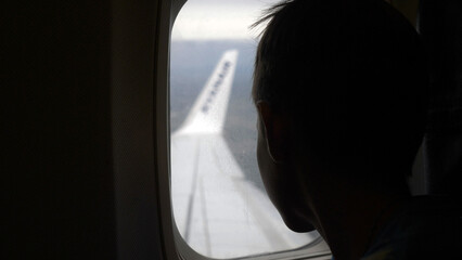 Fototapeta premium boy looks out the porthole during landing airplane, have fun and enjoy