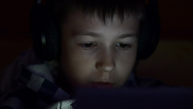 boy plays on the Tablet lying in the dark in headphones, have fun and enjoy