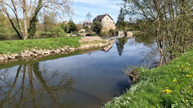 A charming floodgate house next to a tranquil river, with trees and reflections under the bright spring sun