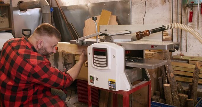 Carpenter occupation. Joinery equipment. Man starting lumber processing in furniture workshop pushing fastened together wood in thickness planer.