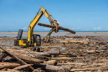 Fototapeta premium Excavator moving debris and logs during post flood cleanup in Padang West Sumatra, highlighting industrial activity, environmental impact, and coastal restoration effort