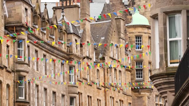 Strings of colorful bunting flags flutter in breeze in front of historic stone buildings with traditional architecture.