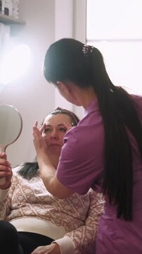 Vertical video. Correction care. Beauty treatment. Professional cosmetologist drawing lines on woman face before plastic procedure.