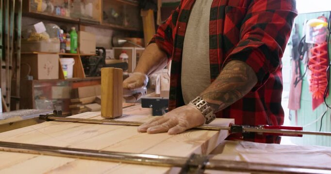 Joinery process. Clamping wood. Carpenter with mallet level part of glued board. Male gloved hands tapping panel set tightened with bar clamps.