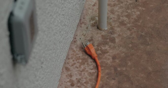 Unplugged Orange Extension Cord on Wet Concrete in Light Rain