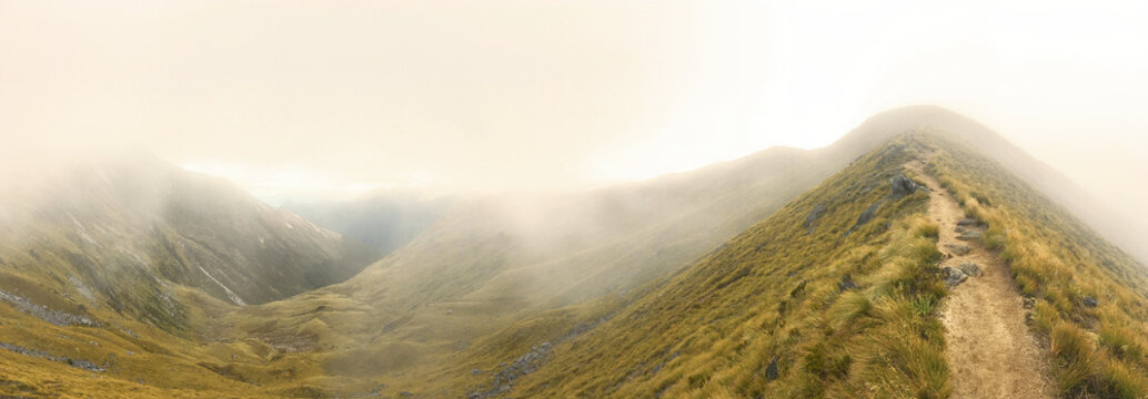 Misty mountain ridge hiking trail panorama - Scenic alpine landscape with winding dirt path through golden meadows and dense fog for travel, adventure, and nature themes