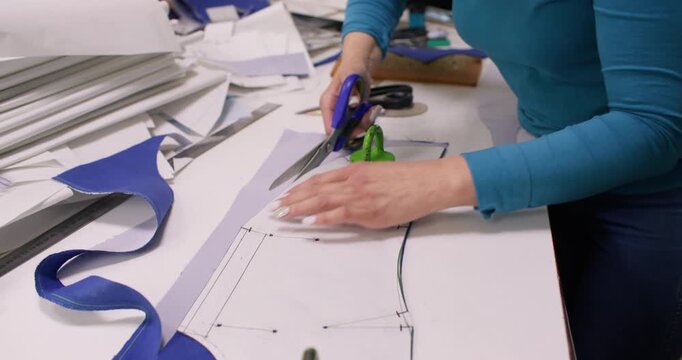 Cutting textile. Atelier work. Woman making pattern with scissors on studio table. Seamstress preparing garment pieces for sewing.
