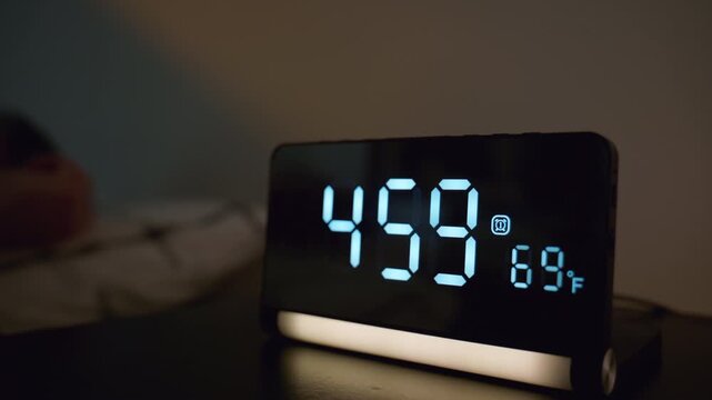 Man turning off alarm clock at 5,00 in bedroom. Early morning wake up moment with digital clock beside bed, hand reaching to stop alarm