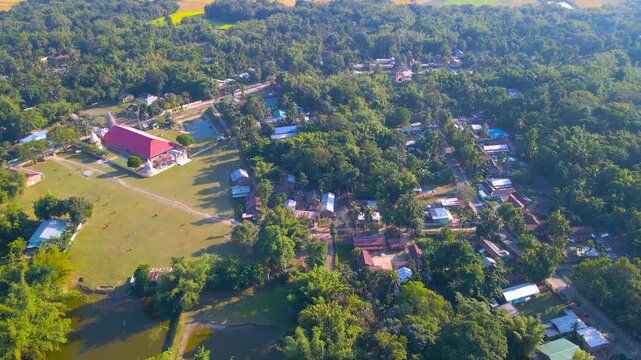 Drone view of Byaskuchi village with houses, grazing animals, and dense tropical greenery in Assam, India.