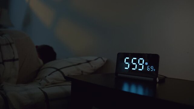 Man turning off alarm clock at 6.00 in bedroom. Early morning wake up moment with digital clock beside bed, hand reaching to stop alarm