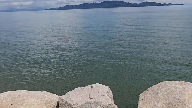 Tilt up, Looking across the calm rippling ocean water with Magnetic Island, Townsville, Queensland in the background, with blue sky and white clouds on a sunny day.