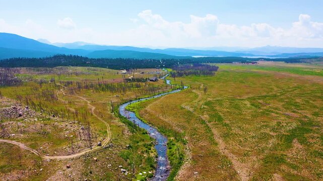 Cinematic drone shot across a Montana river valley featuring a meandering creek open rangeland sparse trees rustic crossings distant blue ridges and sweeping western summer scenery