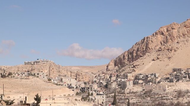 Wide landscape of the historic town of Ma'aloula, Syria, situated at the foot of massive rocky cliffs. A unique cultural and religious site in the mountains