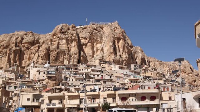 Wide panoramic view of Ma'aloula, Syria, with houses built into the rocky mountainside. Famous Christian village and historic pilgrimage site in the cliffs
