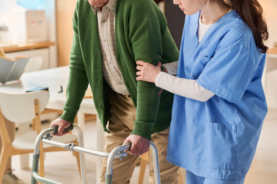Senior man using walker while young adult woman caregiver supporting mobility during rehabilitation. Ideal for elder care, healthcare, recovery support marketing