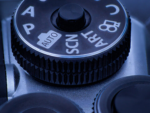 Macro close up of camera mode dial showing auto and scene settings with textured grip detail and cool lighting