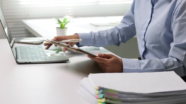 Asian businesswoman reviewing financial documents and using a calculator at her desk. Professional accountant working on a report.