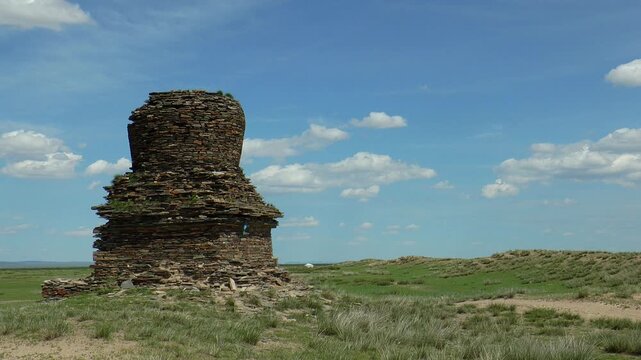 An ancient stupa in the Mongolian steppe against a blue cloudy sky.  