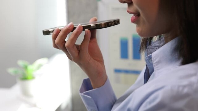 Asian businesswoman recording voice message on smartphone.