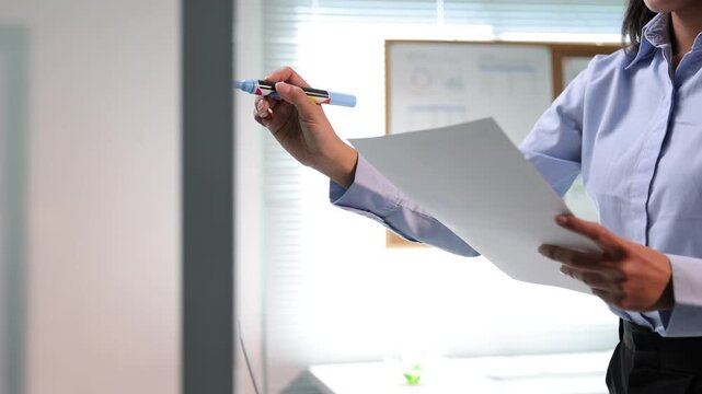 Young businesswoman business strategy on a glass board. Asian professional drawing a mind map on a clear whiteboard. A business manager outlining a new project development plan in the office.