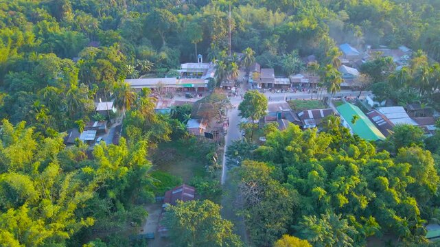 Drone view of road lined with houses, shops, and trees in Byaskuchi village, Assam, India.
