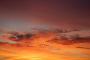 Fototapeta premium Evening sky displaying a beautiful blend of fiery colors from orange and red to soft yellow and purple, with delicate cloud formations enhancing the tranquil and dramatic ambiance of dusk