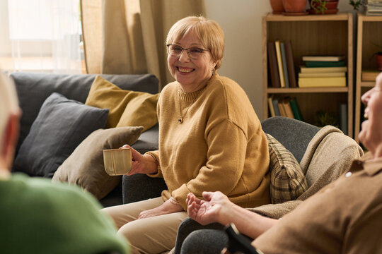 Portrait of senior Caucasian woman smiling and holding mug while talking with peers in recreation room, representing social connection and active aging. Ideal for senior care marketing