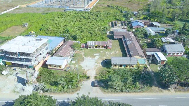 Aerial view of a rural school campus in Assam surrounded by buildings and green fields. Peaceful daylight scene reflects calm village learning environment.