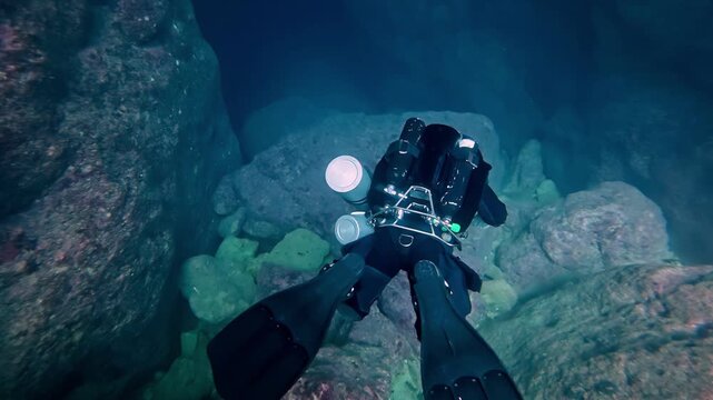 Deep blue adventure of professional technical scuba diver exploring mysterious underwater rock formations and narrow cave passages during summer in crystal clear ocean water with wide low angle view