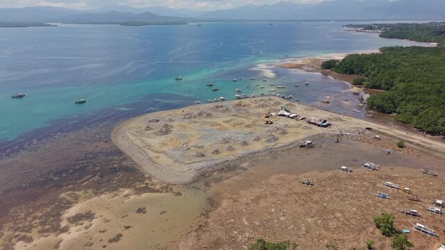 Aerial view of an active coastal land reclamation site in Bankao-Bankao Puerto Princesa Palawan Philippines with rocks construction equipment mangroves and parked outrigger banca boats.