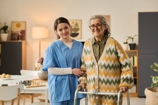 Portrait of senior Caucasian woman using walker with young adult female caregiver standing beside her, supporting mobility and home care. Ideal for eldercare, assisted living, caregiving marketing