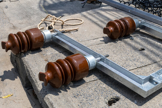 Three brown ceramic insulators on a metal frame lie on concrete, ready for use in electrical infrastructure maintenance and wire replacement in Thailand.