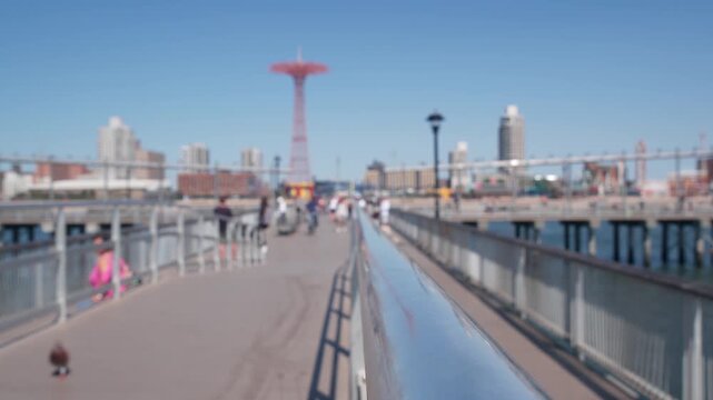 Coney Island beach, wooden pier promenade in Brooklyn, New York, United States. Boardwalk near retro luna park. Amusement park on ocean coast beach. People on waterfront summer holiday in NYC, USA.