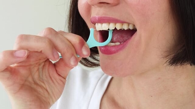 Young Woman Using Blue Plastic Dental Floss Pick on White Healthy Teeth &mdash; Female Interdental Cleaning with Disposable Flosser, Oral Hygiene Daily Routine, Gum Care and Preventive Dentistry