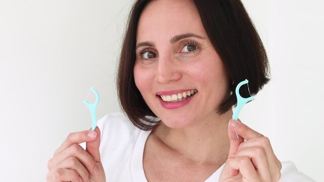Young Woman Using Blue Plastic Dental Floss Pick on White Healthy Teeth &mdash; Female Interdental Cleaning with Disposable Flosser, Oral Hygiene Daily Routine, Gum Care and Preventive Dentistry
