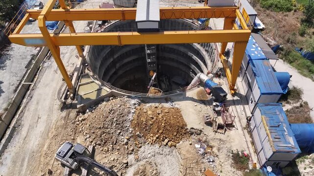 Massive gantry crane transporting excavated soil from a metro shaft. High angle operational shot of deep excavation systems, bored pile walls, and site logistics cycle.