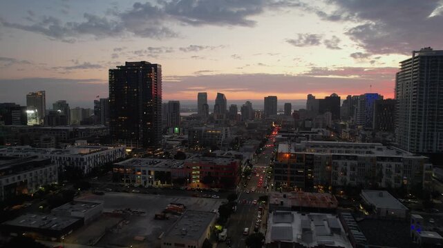 Forward-moving drone approaching downtown San Diego skyline at 8PM during sunset with warm glowing light.
