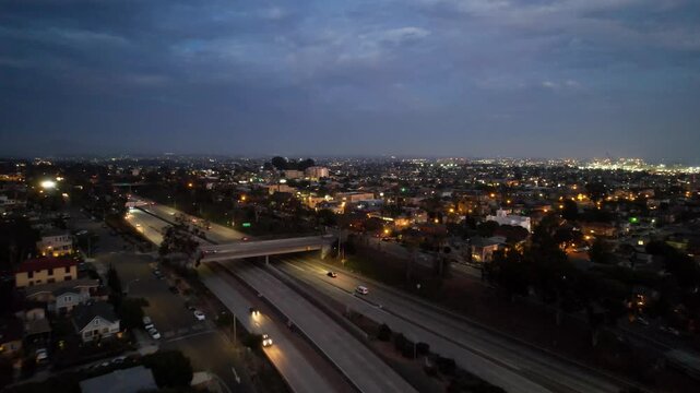 Drone flying southeast across freeway traffic near downtown San Diego at 8PM during sunset with active city movement.
