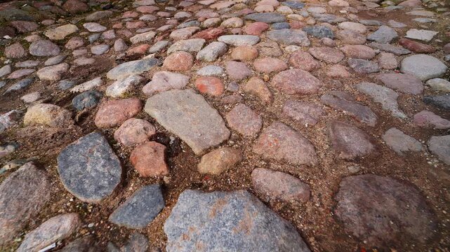 Close-up of uneven historic cobblestone ground with rounded fieldstones and sandy gaps, highlighting aged street texture, rough footing, and old town pavement detail.