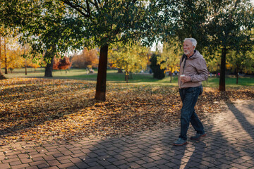 Fototapeta premium Senior man walking with coffee in autumn park