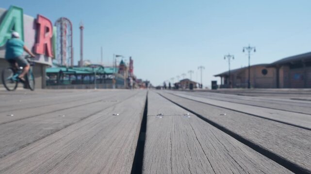 Coney Island beach promenade in Brooklyn, New York, United States. Wooden boardwalk near retro luna park. Amusement park on ocean coast beach. Waterfront summer holiday, people walking on promenade.