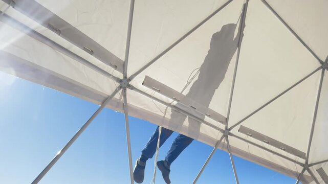 Worker assembling a white geodesic dome tent against a blue sky
