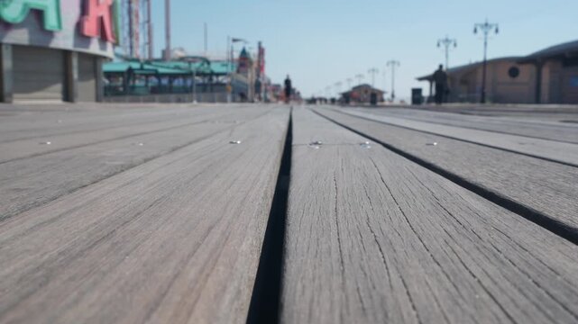 Coney Island beach promenade in Brooklyn, New York, United States. Wooden boardwalk near retro luna park. Amusement park on ocean coast beach. Waterfront summer holiday, people walking on promenade.