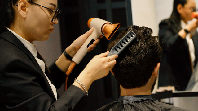 Professional barber drying hair and styling for young male client
