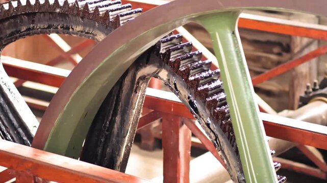 Large industrial gears turn slowly showing metal teeth and oil in vintage machinery close-up.